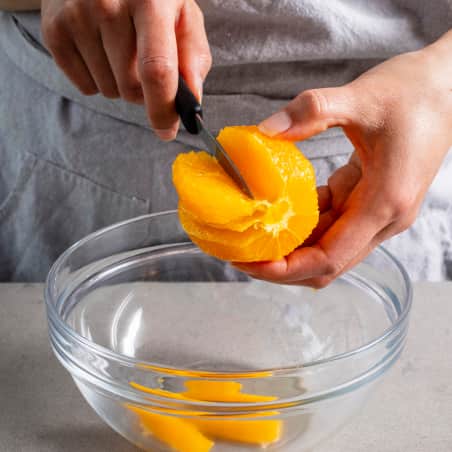 Hands holding a peeled orange and a paring knife making cuts in it